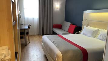 A hotel room with a bed, a desk, a chair, a sofa, and a window with curtains.