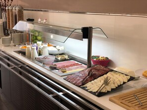 A buffet with various food items, including meats, cheeses, and fruits.