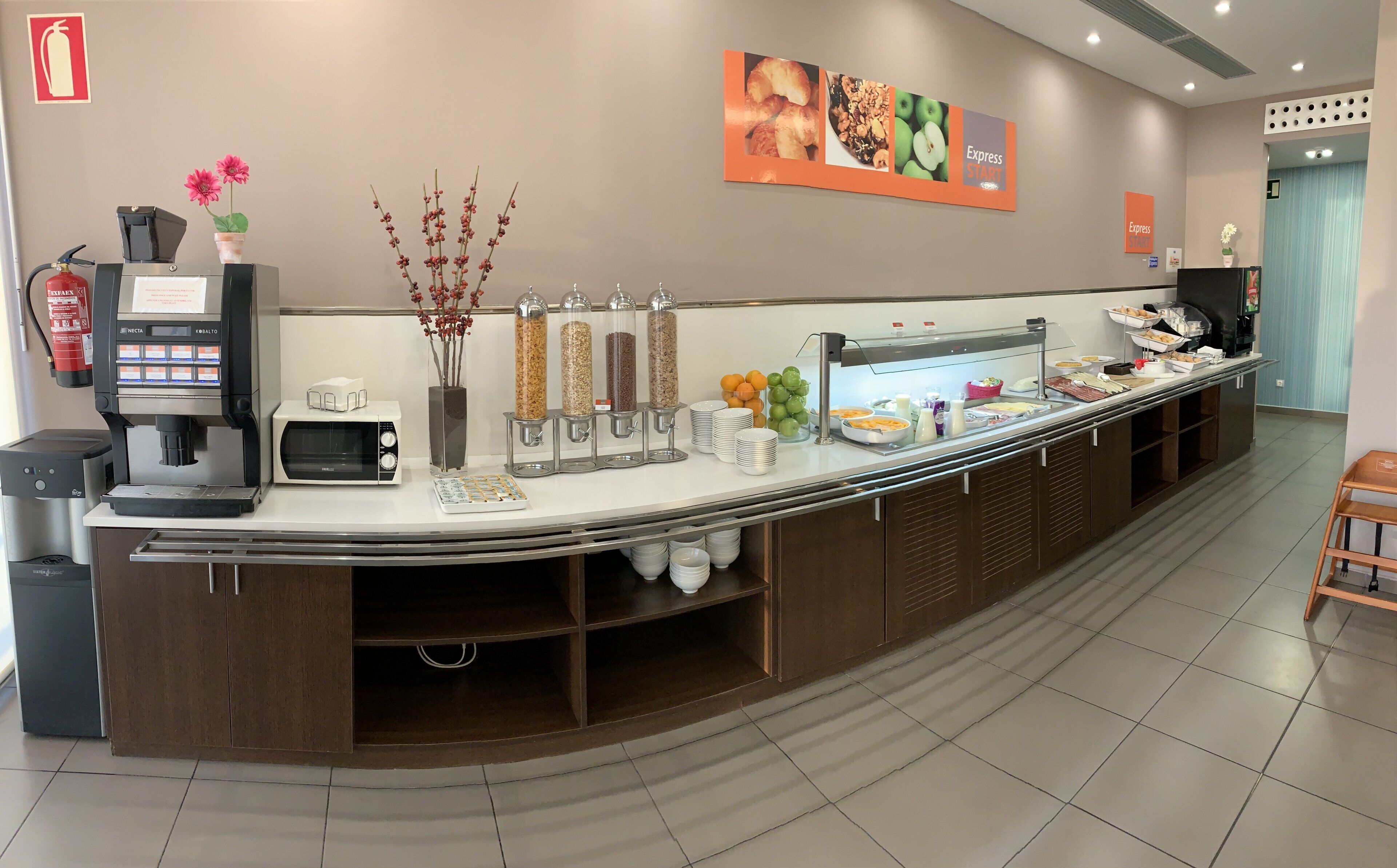 Een ontbijtbuffet met een koffieapparaat, magnetron en diverse soorten eten.