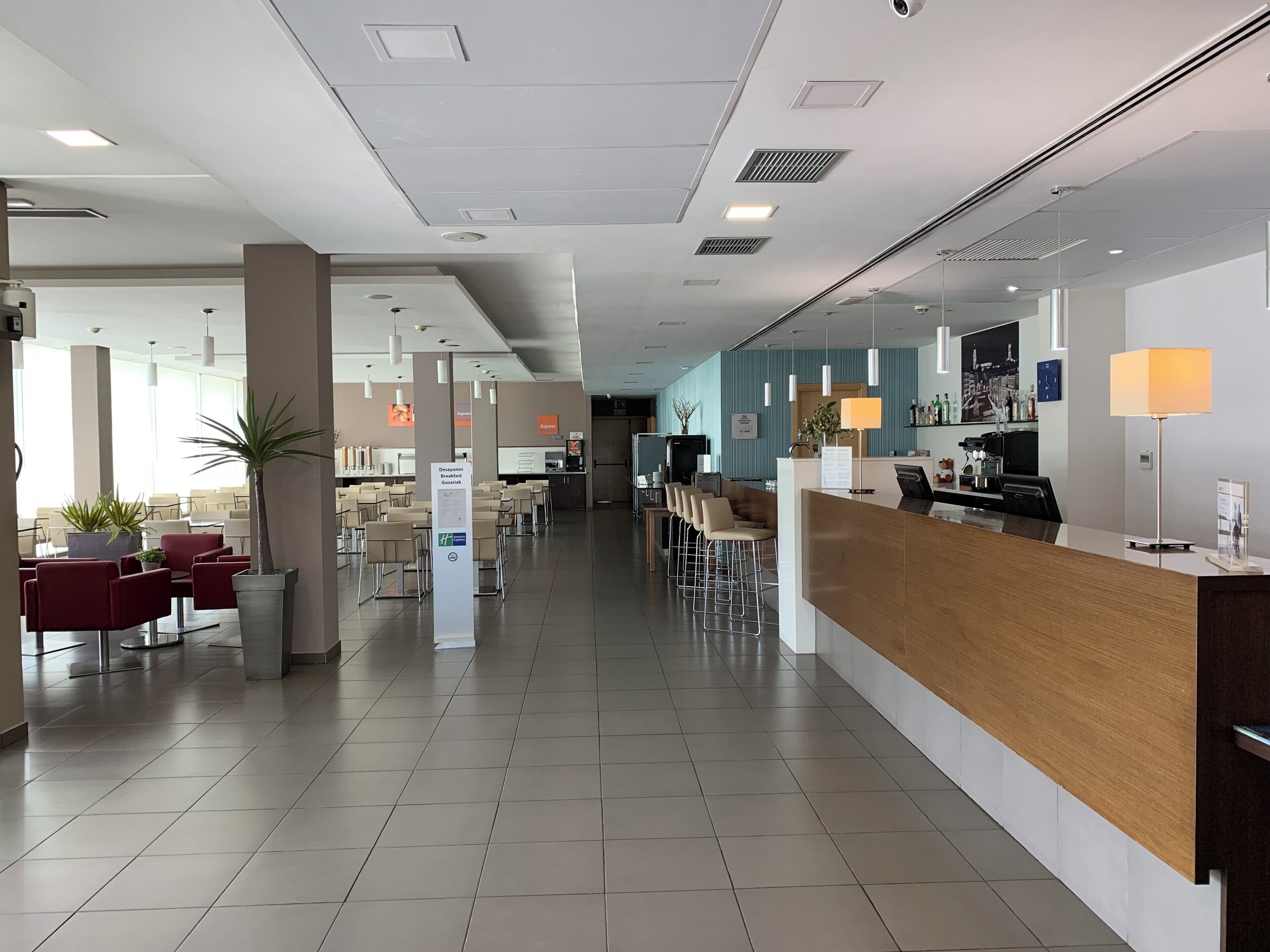 A modern hotel lobby with a reception desk, seating area, and a large window providing natural light.