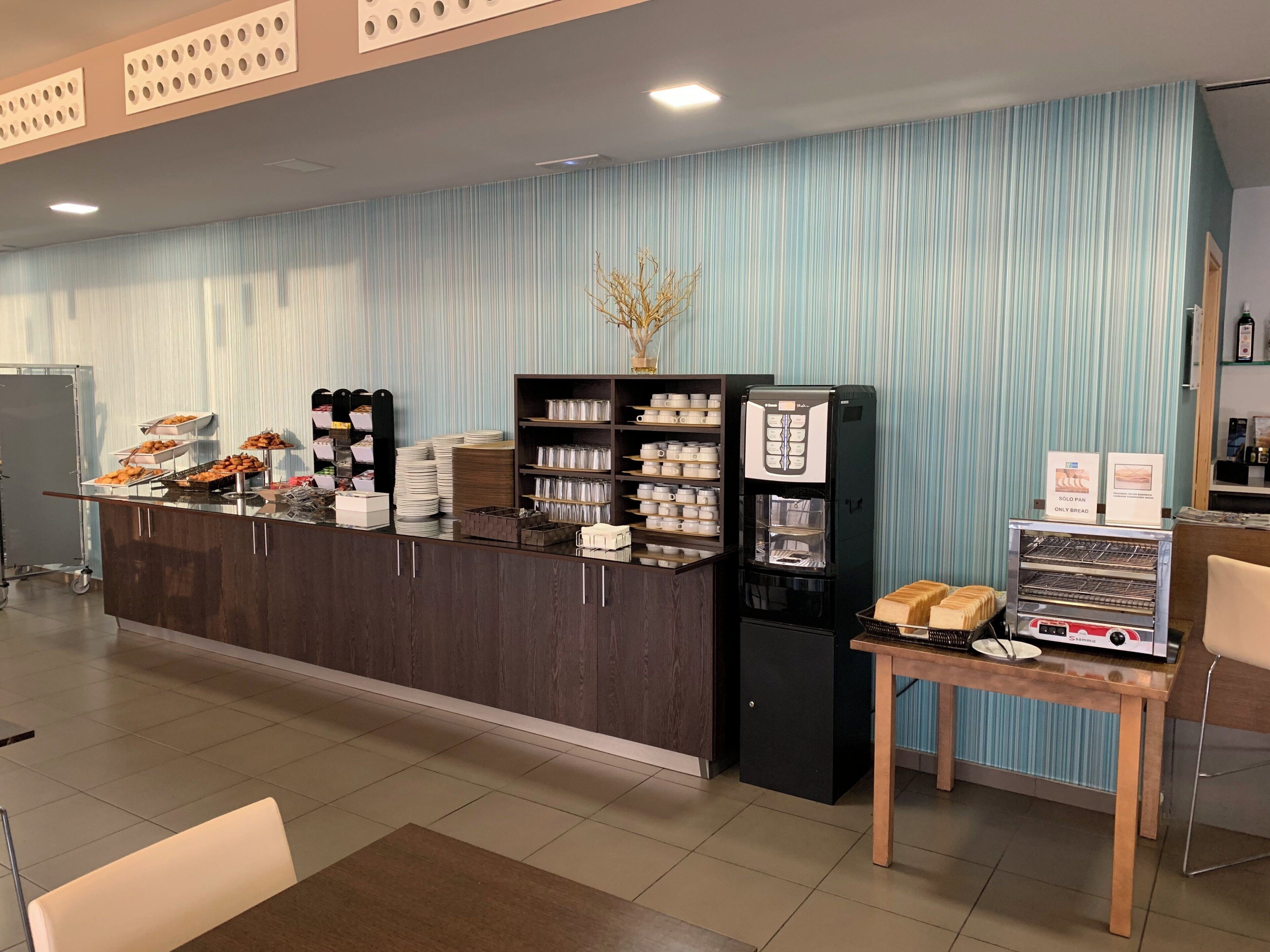 Un área de recepción con un mostrador que exhibe alimentos, una máquina de café y una barra de pan.