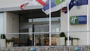 A Holiday Inn Express building with a glass entrance, a stone wall in front, and flags hanging outside.