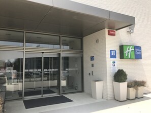 Entrada de un hotel con puerta de vidrio, un letrero que dice 'FUEGO' y el logotipo de Holiday Inn Express.