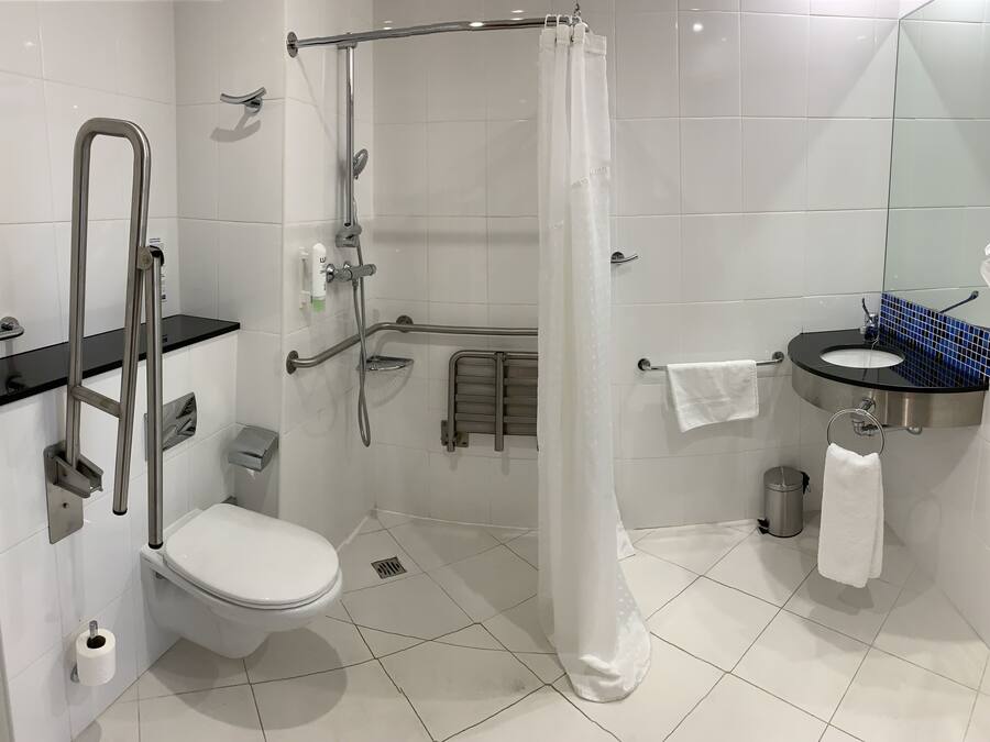 Un baño moderno con cabina de ducha, barras de apoyo, inodoro, lavamanos y espejo.