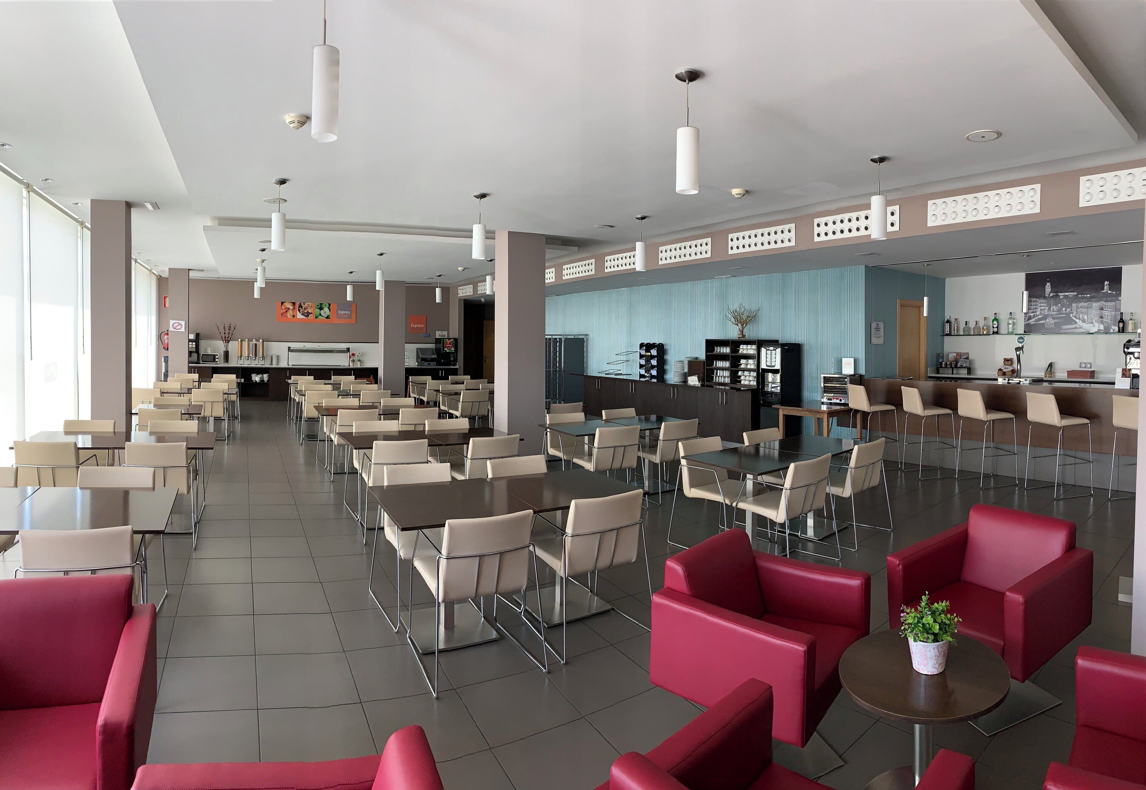 A modern hotel lobby with multiple seating areas, including tables and chairs, and a bar area with a counter and stools.