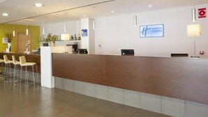 Una zona de recepción con un mostrador de madera, varios taburetes tipo bar, una planta en maceta y un cartel de Holiday Inn Express en la pared.