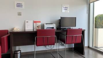 A business corner with a desk, two red chairs, a computer, a telephone, and a trash bin.