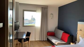 Habitación de hotel con cama, escritorio, silla, sofá y ventana con vista a un edificio.