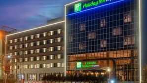 A Holiday Inn Express hotel with a modern glass facade, multiple floors, and illuminated signage. - Holiday Inn Express Tianjin Dongli by IHG (Tianjin)