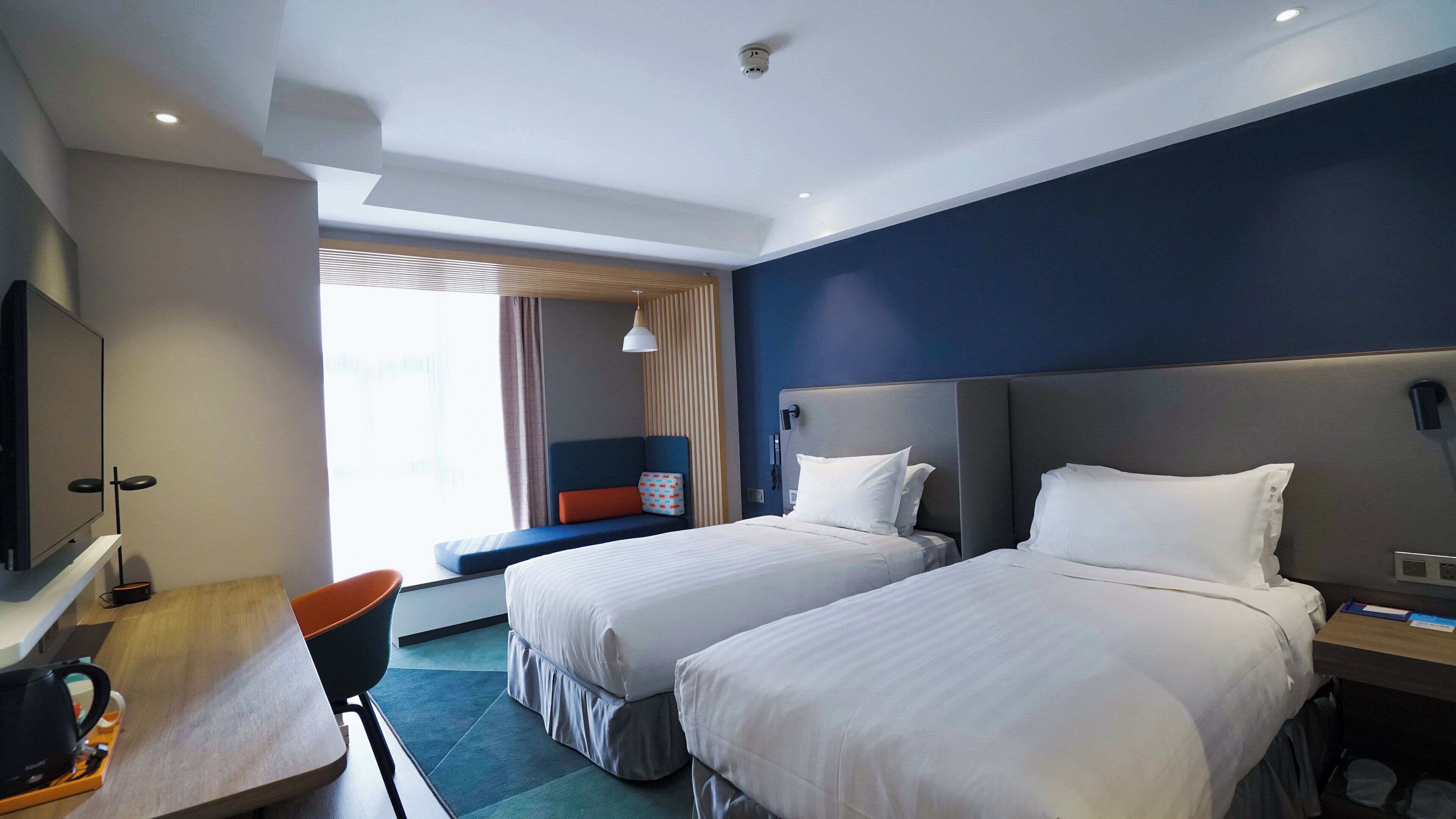 A hotel room with two beds, a desk with a chair, a TV, and a window with curtains.