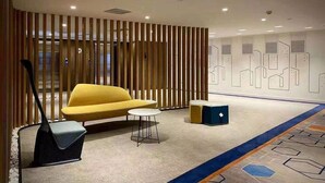 A modern lobby with a yellow sofa, a small round table, a black bench, and a decorative wall with geometric patterns. - Holiday Inn Express Tianjin Dongli by IHG (Tianjin)