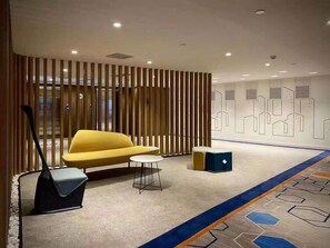 A modern lobby with a yellow sofa, a small round table, a black bench, and a decorative wall with geometric patterns. - Holiday Inn Express Tianjin Dongli by IHG (Tianjin)