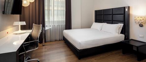 Une chambre d’hôtel moderne équipée d’un lit, d’un bureau, d’une chaise et d’un téléviseur fixé au mur.