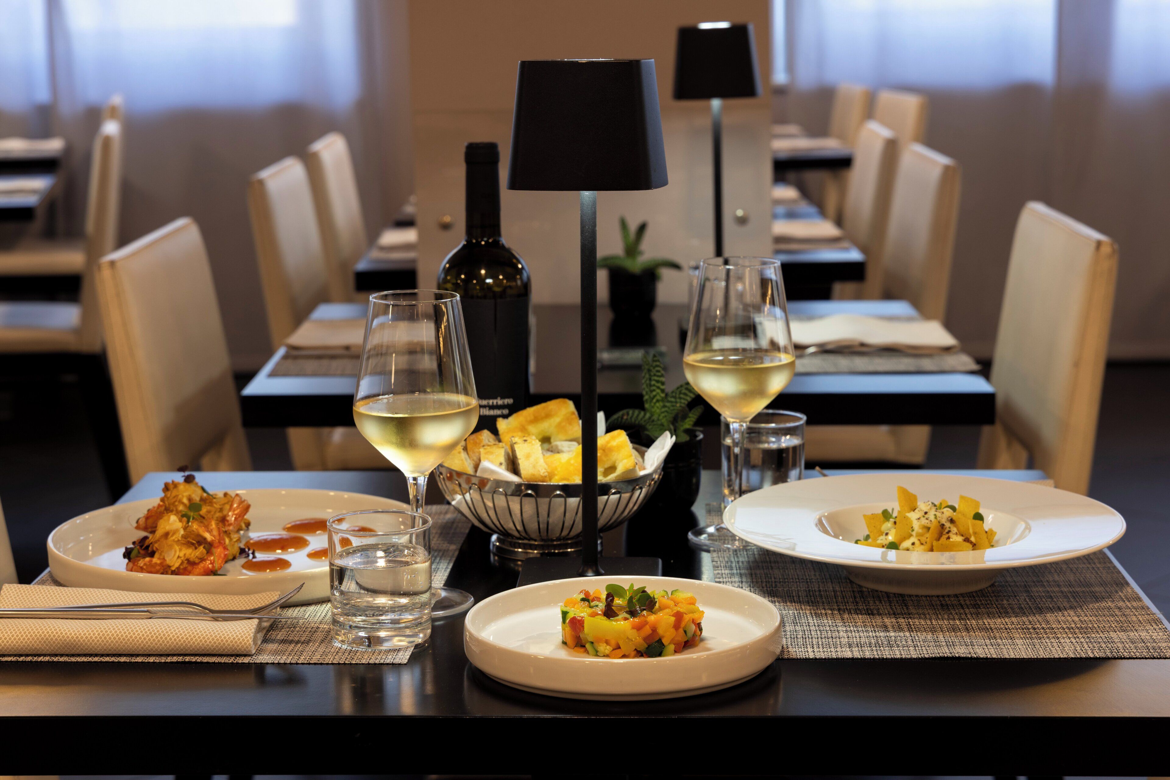 A dining table with plates of food, glasses of wine, and a bottle of wine.
