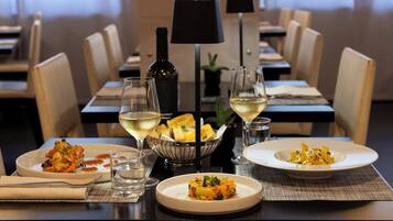 A dining table with plates of food, glasses of wine, and a bottle of wine.
