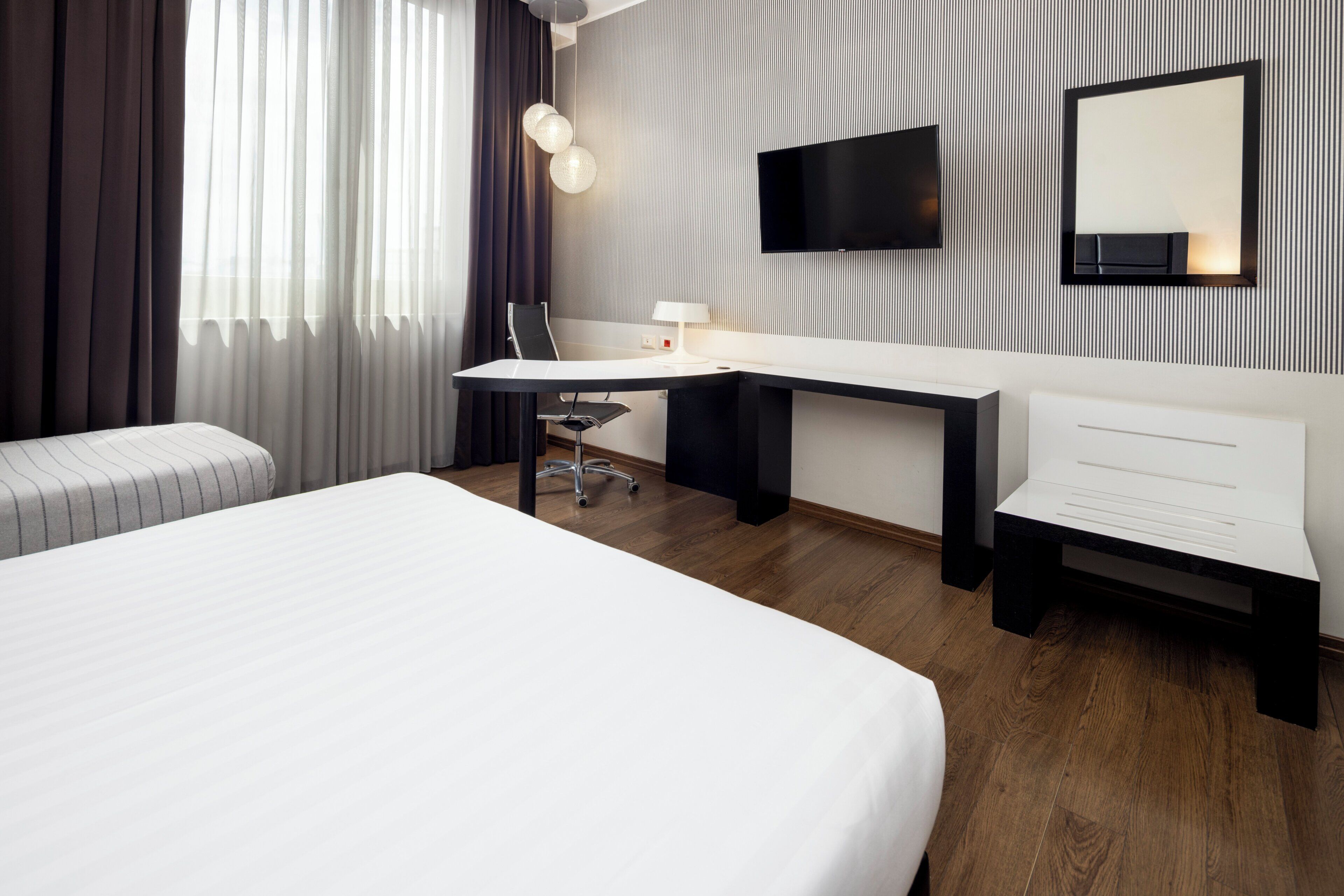 Ein modernes Hotelzimmer mit einem großen Bett, einem Schreibtisch mit Stuhl, einem an der Wand befestigten Flachbildfernseher und einem Nachttisch.