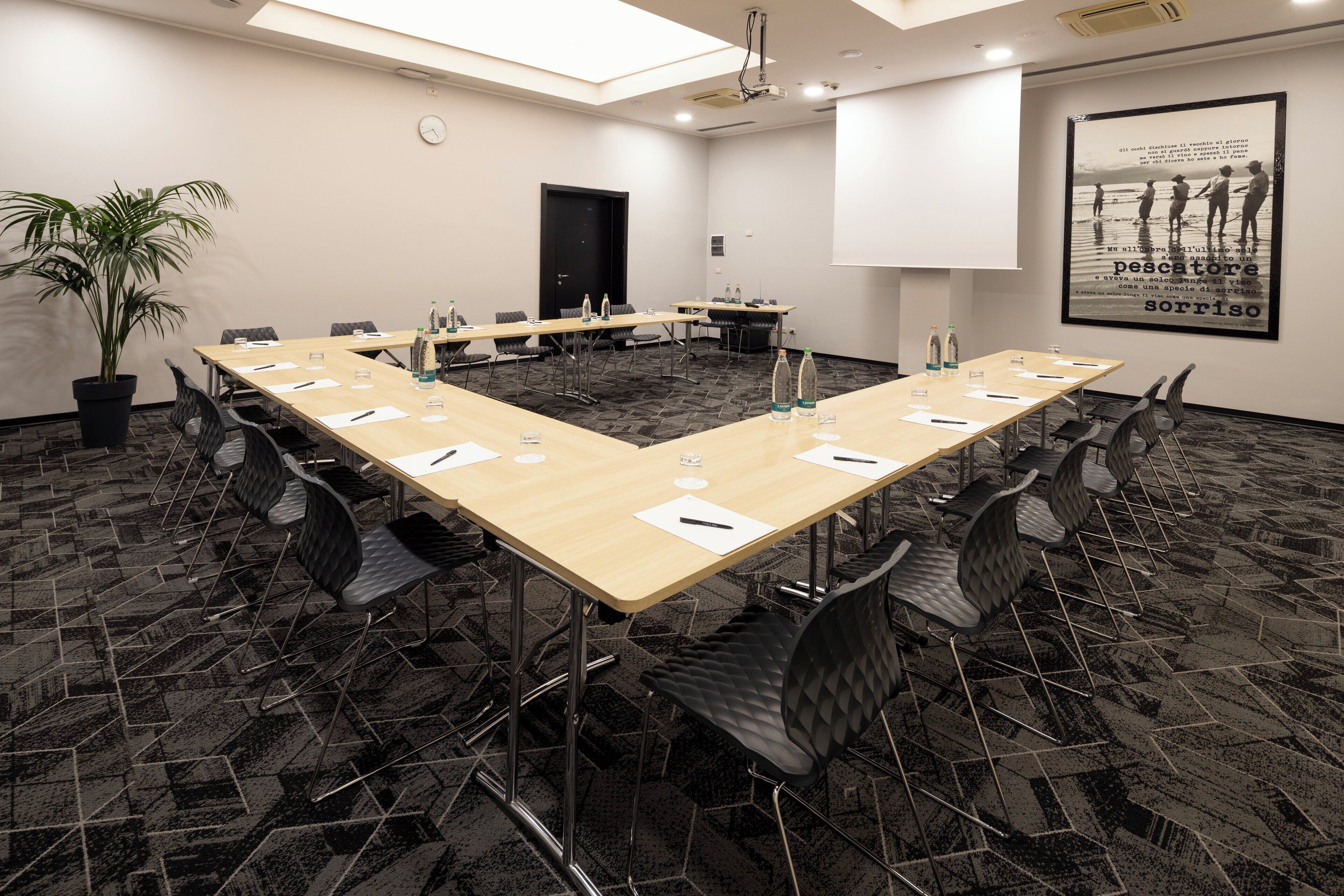 A conference room with a long table, chairs, water bottles, and a clock on the wall.