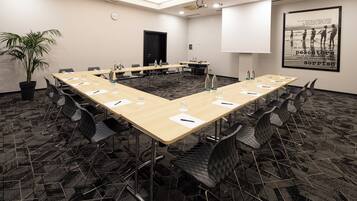 Une salle de conférence avec une longue table, des chaises, des bouteilles d’eau et une horloge au mur.