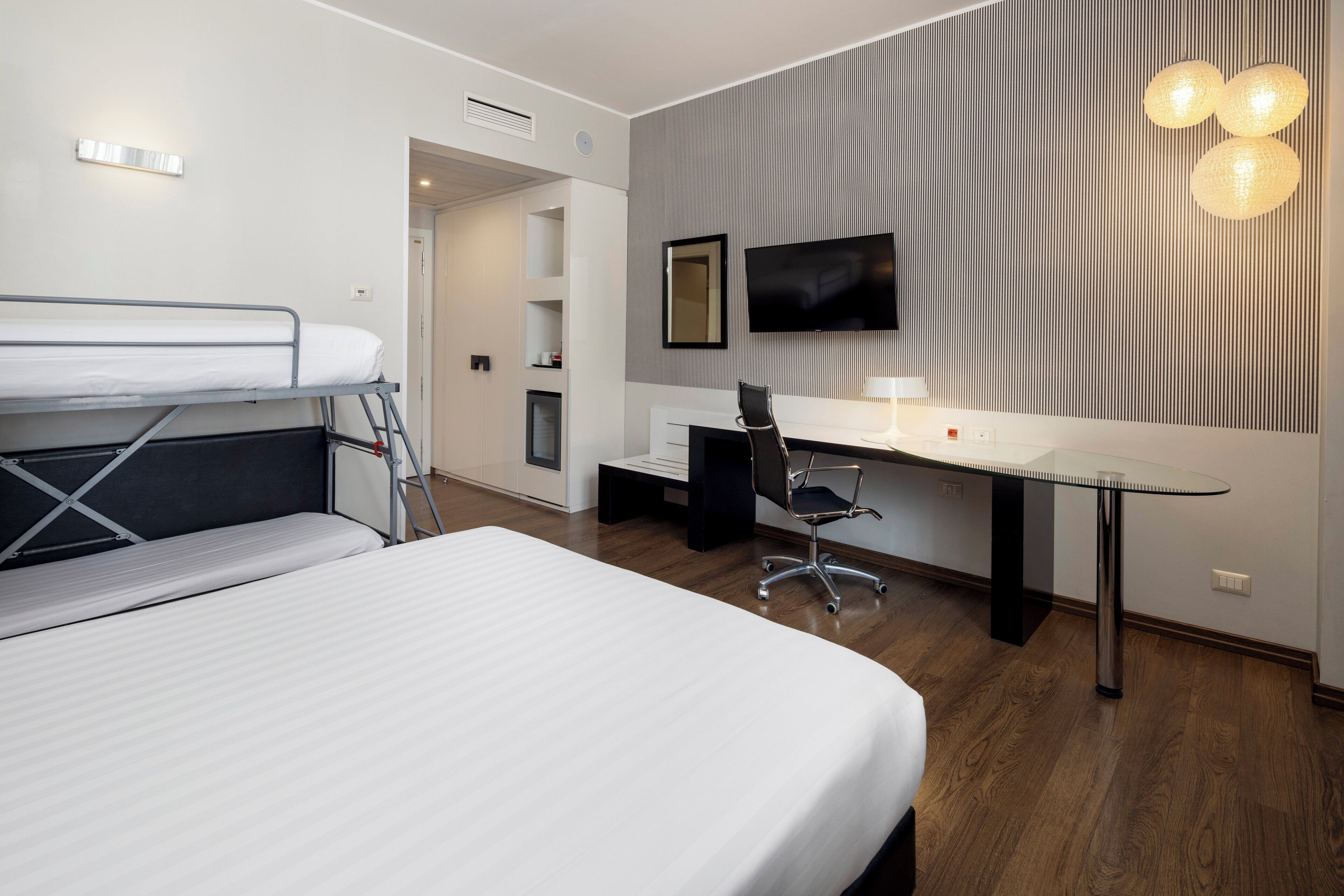 Una habitación de hotel moderna con una cama litera, un escritorio, una silla y un televisor montado en la pared.