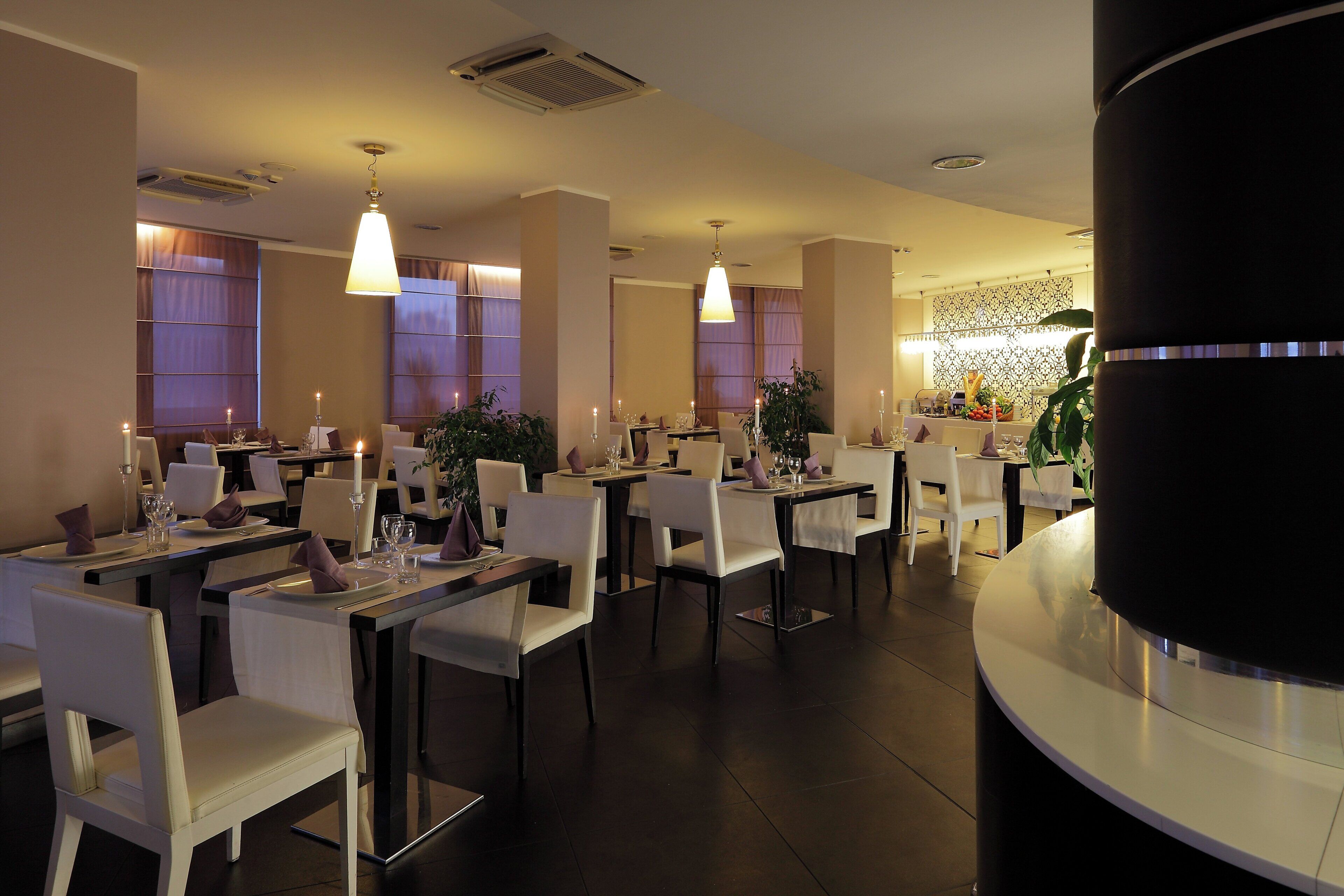 A restaurant interior with multiple dining tables, chairs, and pendant lighting.