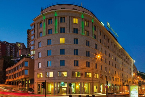 Un hôtel à plusieurs étages, doté d’une façade incurvée, de fenêtres illuminées et d’une enseigne bien visible indiquant qu’il s’agit d’un Holiday Inn.