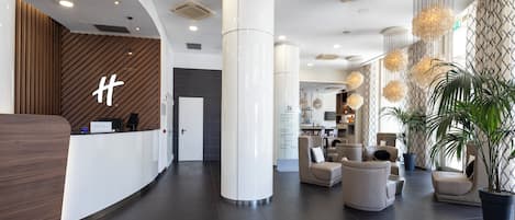 A modern hotel lobby with a reception desk, seating area, and a large potted plant.
