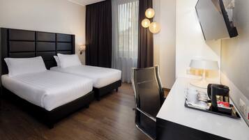 Ein Hotelzimmer mit zwei Betten, einem Schreibtisch mit Lampe und einer Kaffeemaschine.