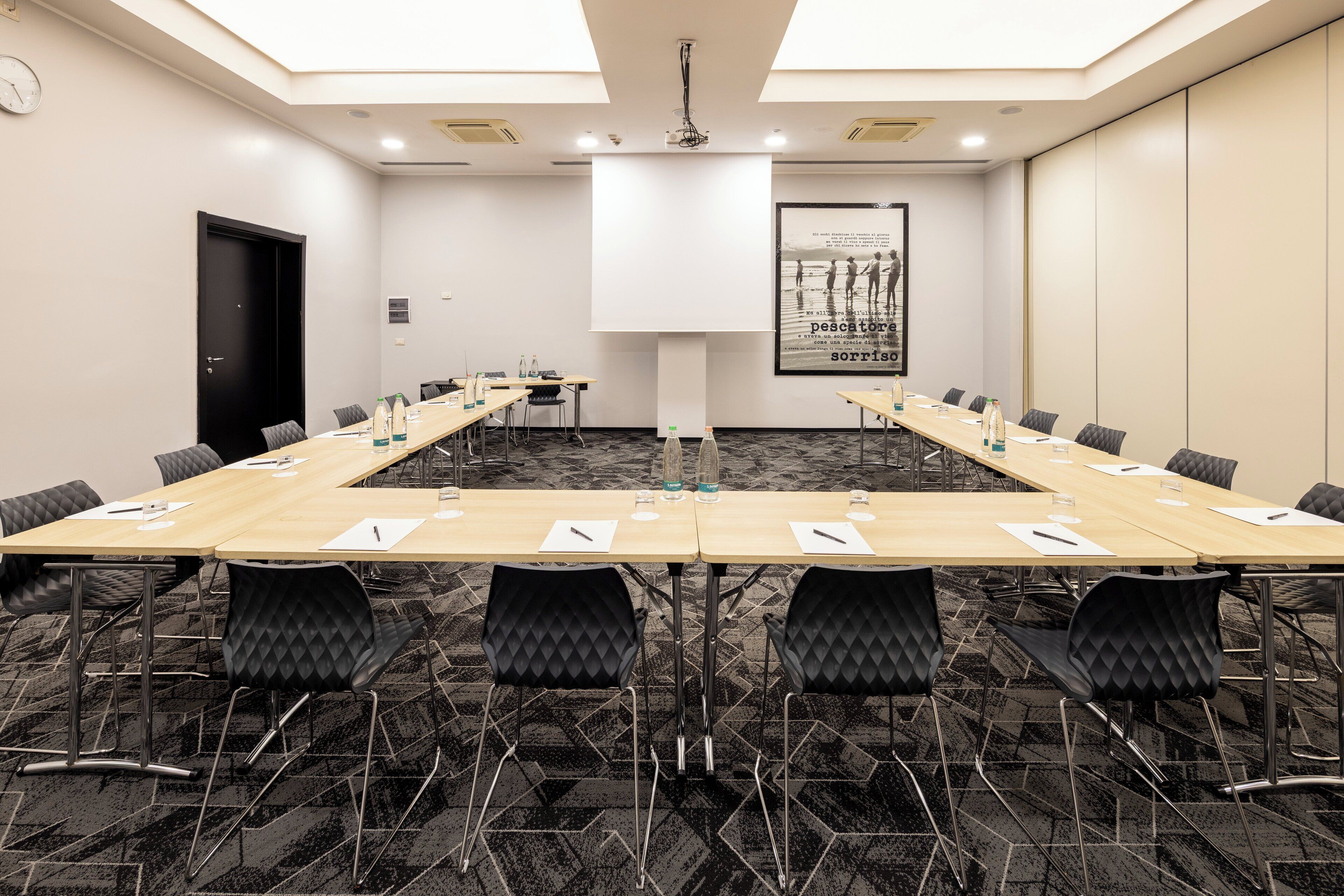 A conference room with a long table, chairs, and a projector screen.