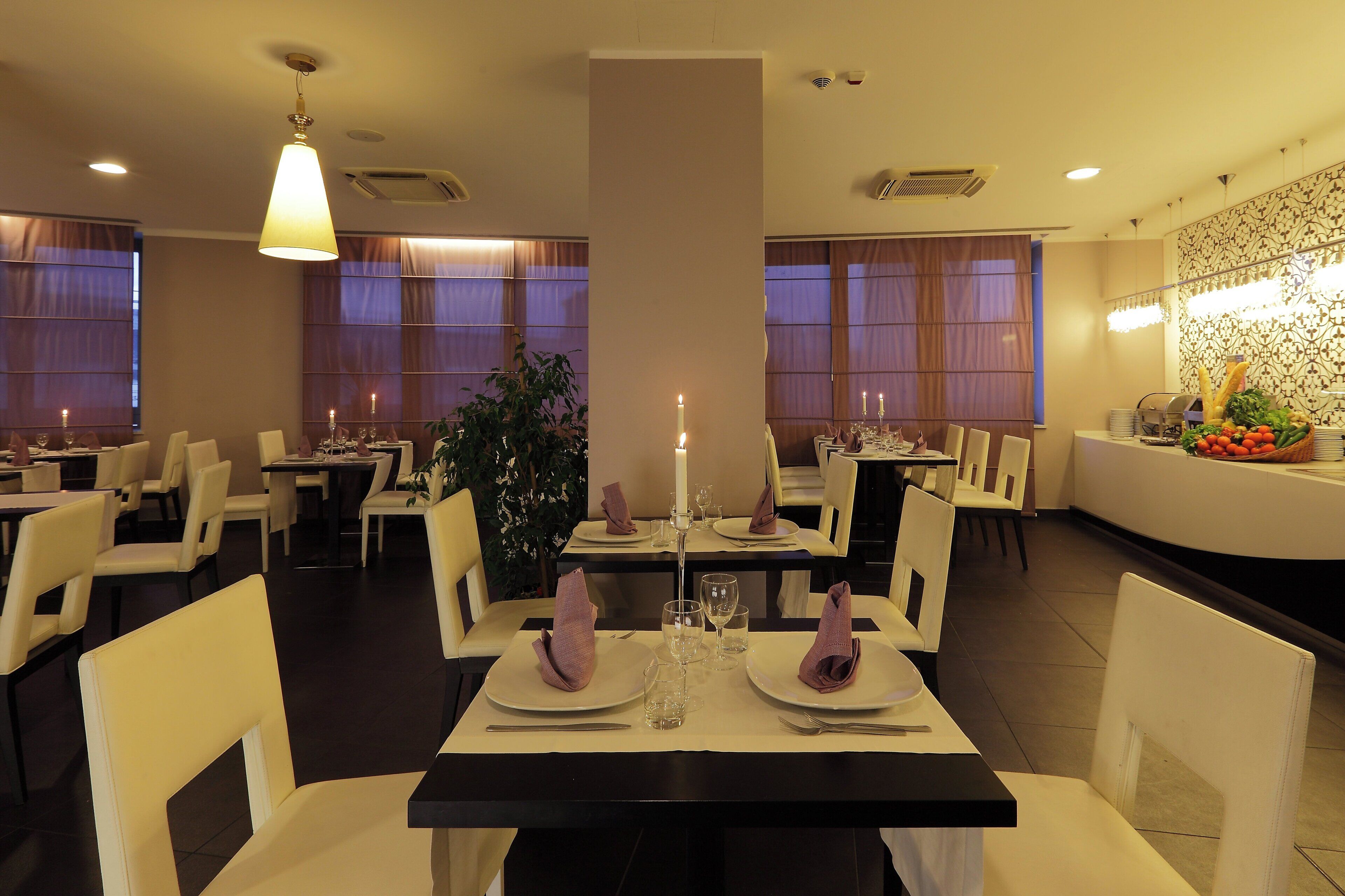 A restaurant with tables set for dining, featuring a central plant and candles.