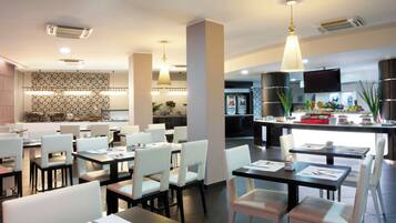 A modern dining area with tables and chairs, a kitchen in the background, and a buffet counter with food items.