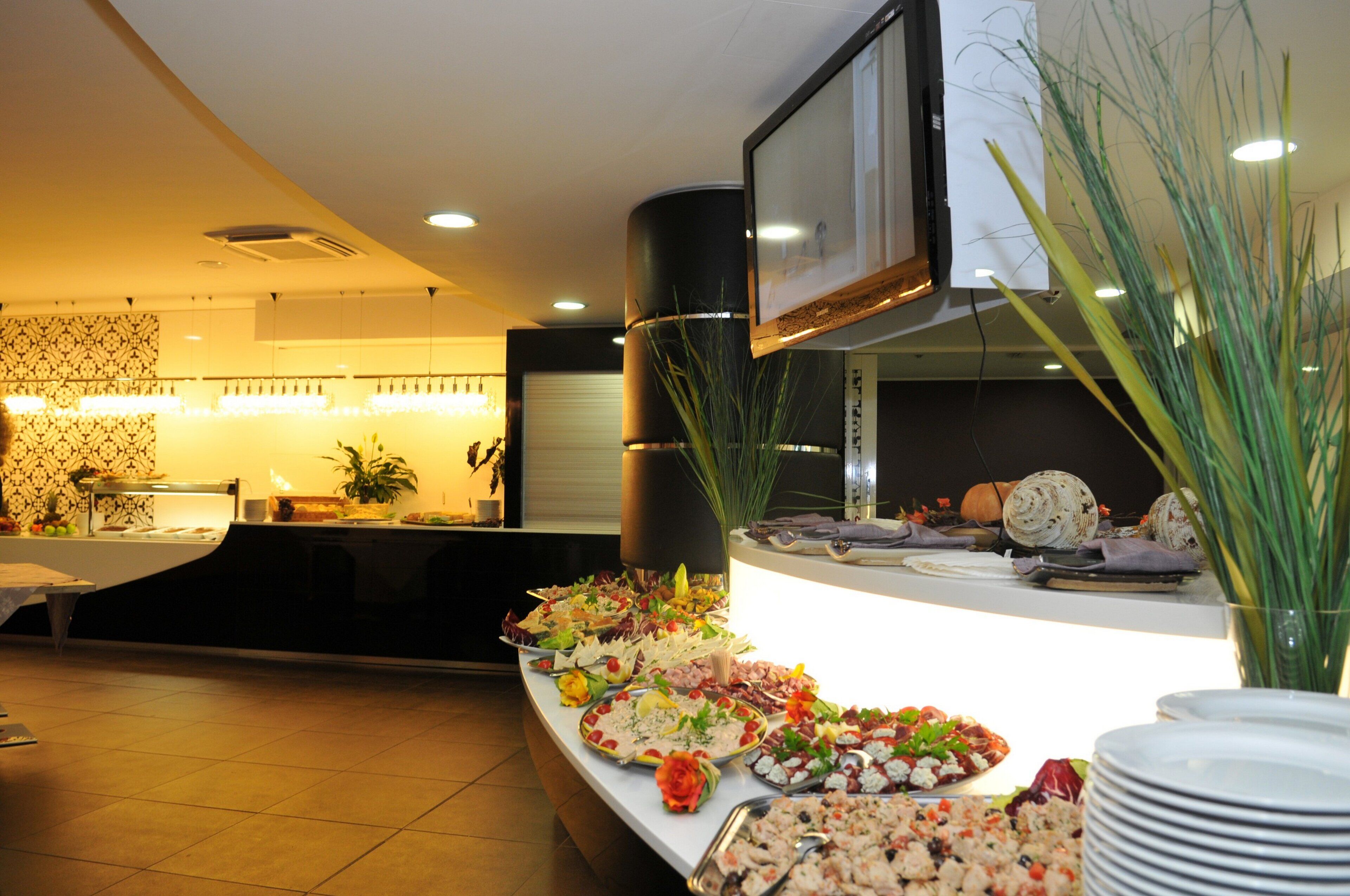 A buffet setup with various food items and a television screen mounted on the wall.