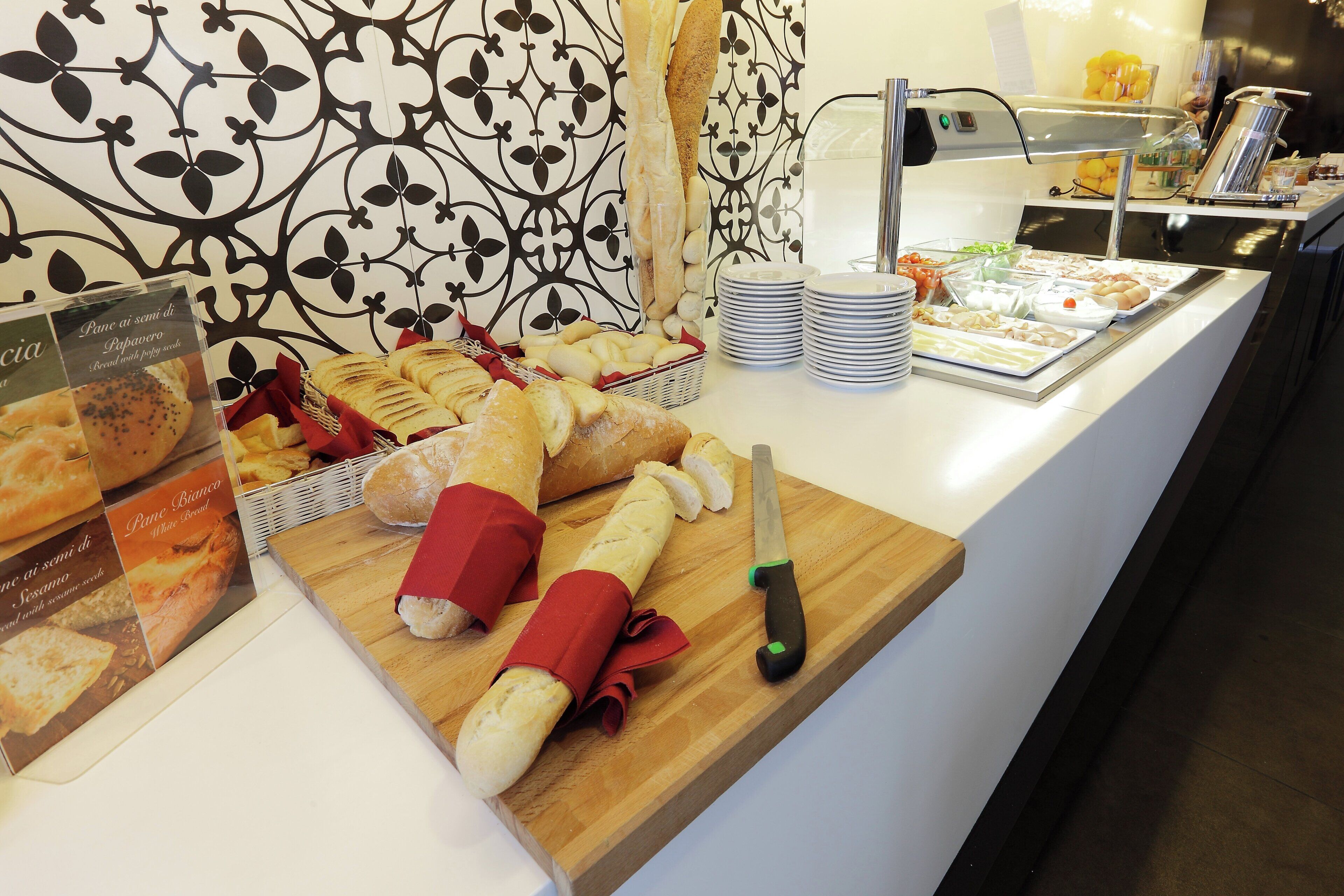 A buffet counter with various bread and pastries, a knife, and a stack of plates.