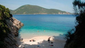 Una playa con agua turquesa cristalina, acantilados rocosos y un paisaje montañoso al fondo.