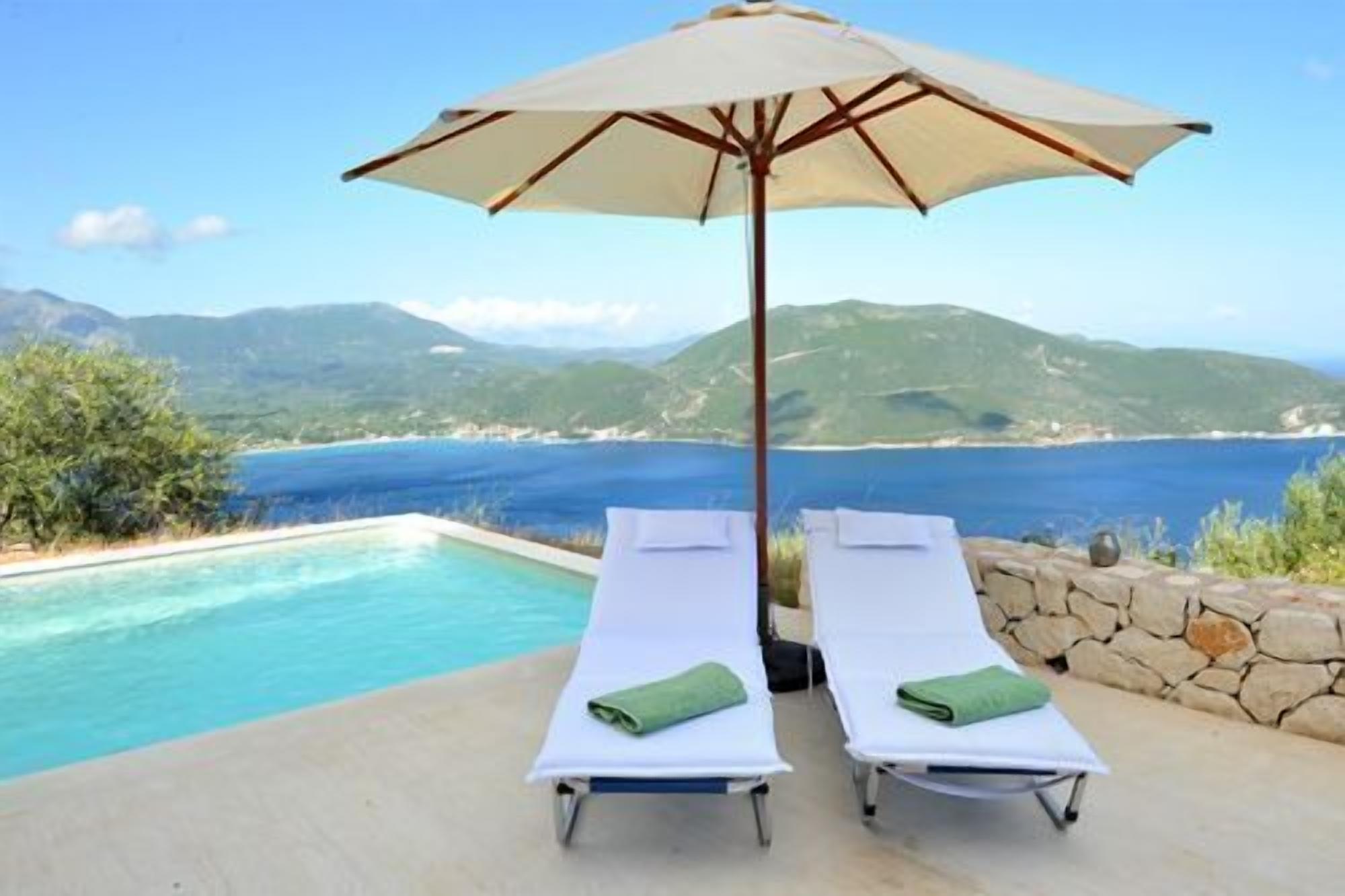 Deux chaises longues avec des serviettes vertes, un parasol et une piscine donnant sur un paysage côtier.