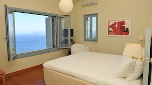 Un dormitorio con una cama grande, un ventanal con vista al mar, una lámpara en el techo y un aire acondicionado instalado en la pared.