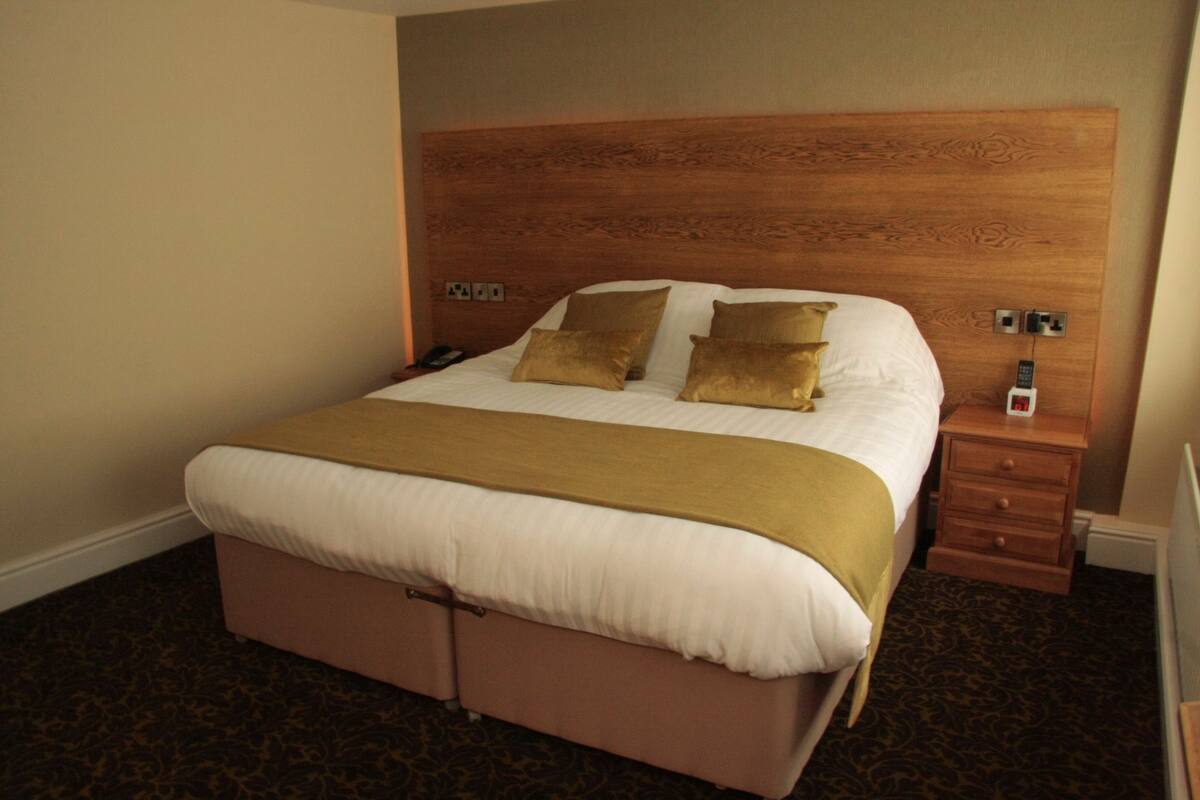 A hotel room with a large bed, wooden headboard, bedside tables, and a telephone.