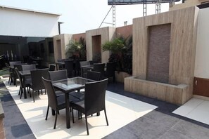 An outdoor patio area with multiple tables and chairs, a concrete wall with a built-in planter, and a ladder in the background. - Hotel Chanchal Deluxe (New Delhi)