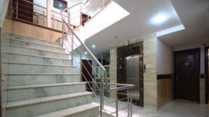 A modern interior with marble stairs, a glass railing, and a marble elevator. - Hotel Chanchal Deluxe (New Delhi)