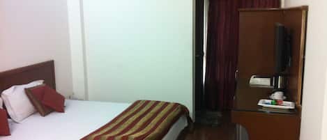 A hotel room with a bed, a TV, a desk with a coffee maker, and a window with curtains.