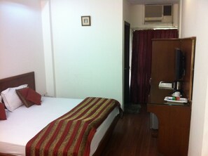A hotel room with a bed, a TV, a desk with a coffee maker, and a window with curtains. - Hotel Chanchal Deluxe (New Delhi)