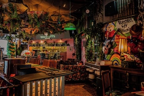Una cafeteria acollidora i eclèctica amb un juke-box antic, barra de cafè i murals colorits.