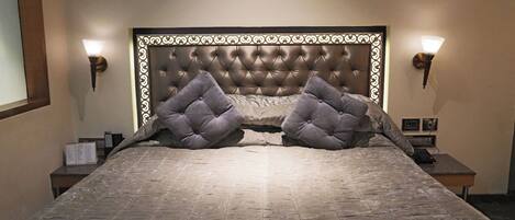 A neatly made bed with a tufted headboard, two bedside lamps, and a small table with a remote control.