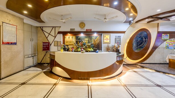A reception area with a curved reception desk, ceiling fans, a clock, and a large decorative wall piece. - Hotel Chanchal Continental (New Delhi)