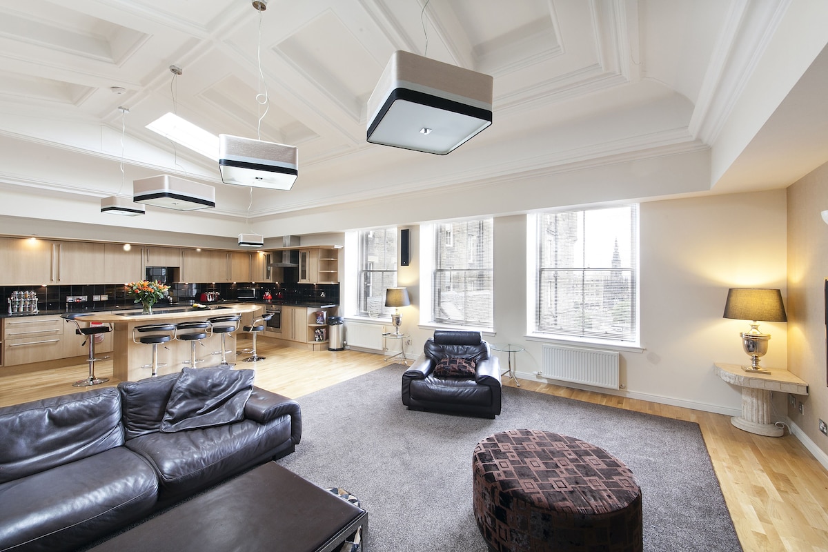 A spacious living area with a modern kitchen, a leather sofa, and a dining area with bar stools.