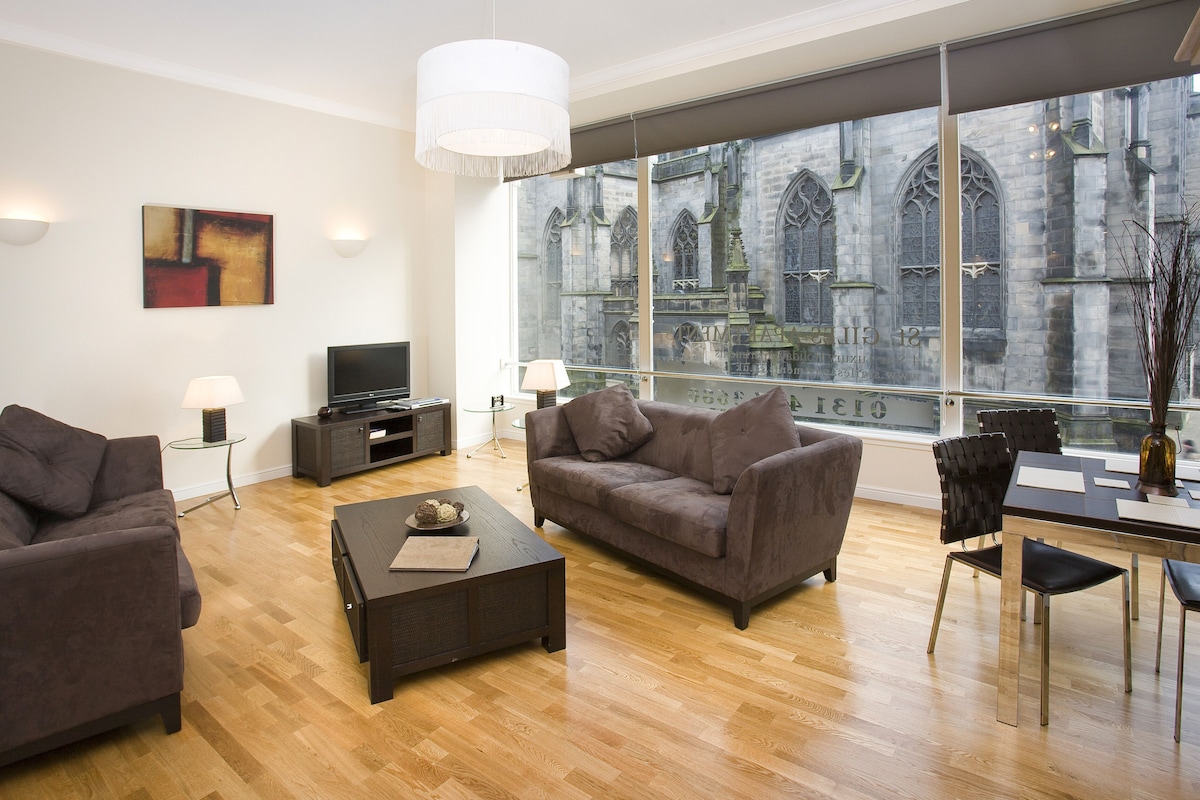A modern living room with a large window, a flat-screen TV, and a dining area with a table and chairs.