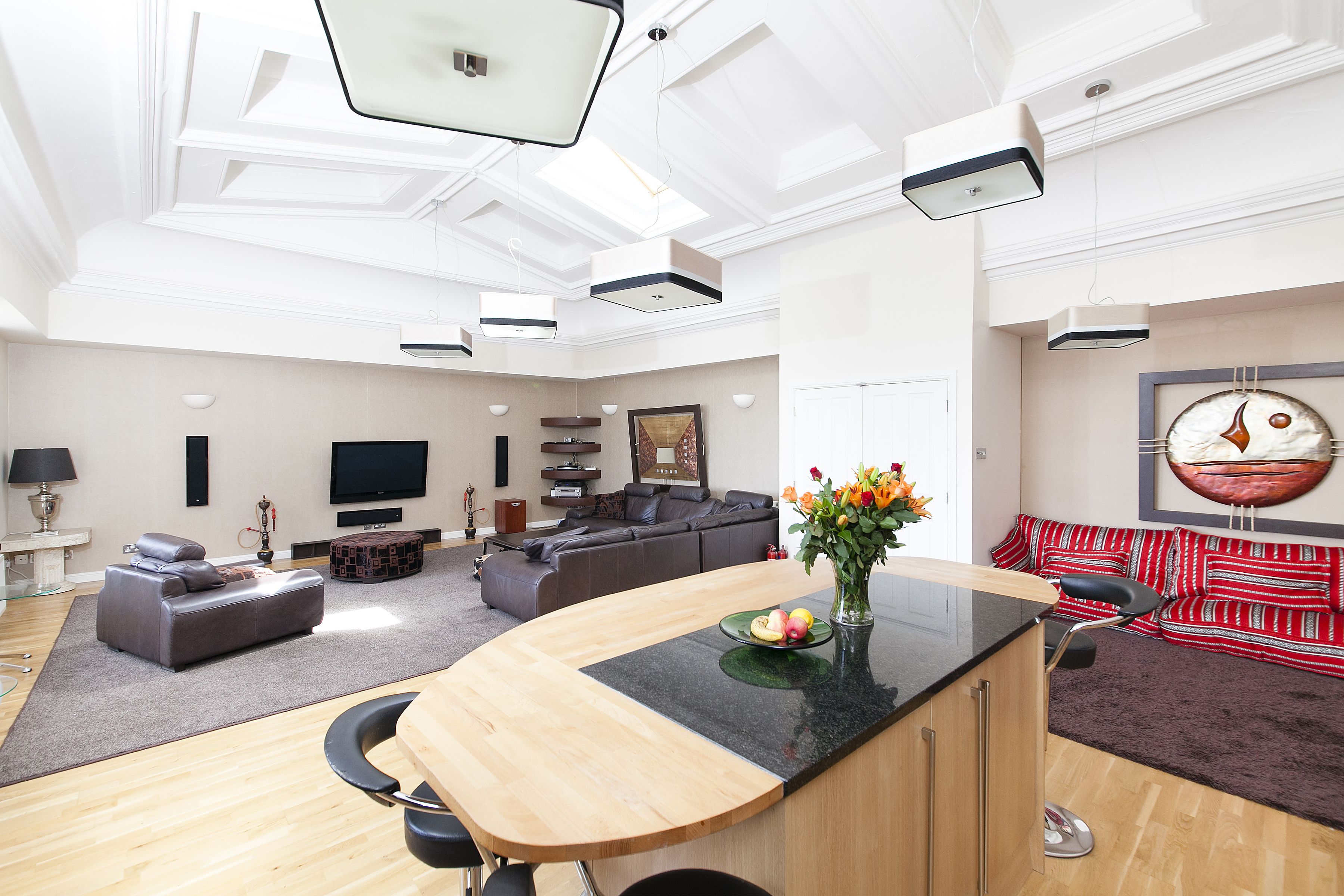 Een moderne woonkamer met een gebogen houten bar, een grijze bank, een bank met een rood-wit patroon, en een flatscreen televisie.