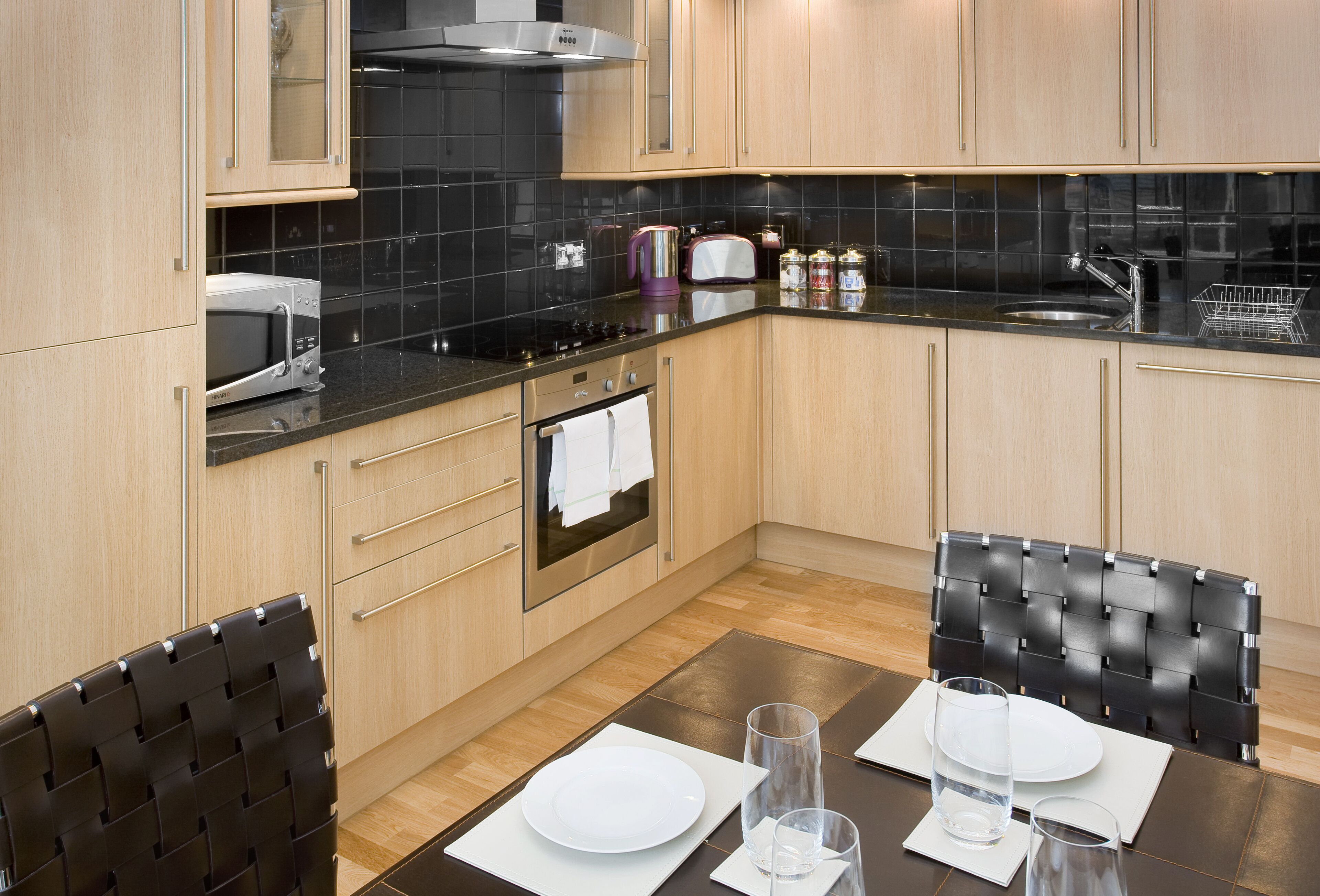A modern kitchen with wooden cabinets, a black countertop, and a dining area with a black chair and a white table set for two.