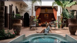 A pool area with a person relaxing, surrounded by potted plants and a dining area with outdoor furniture.