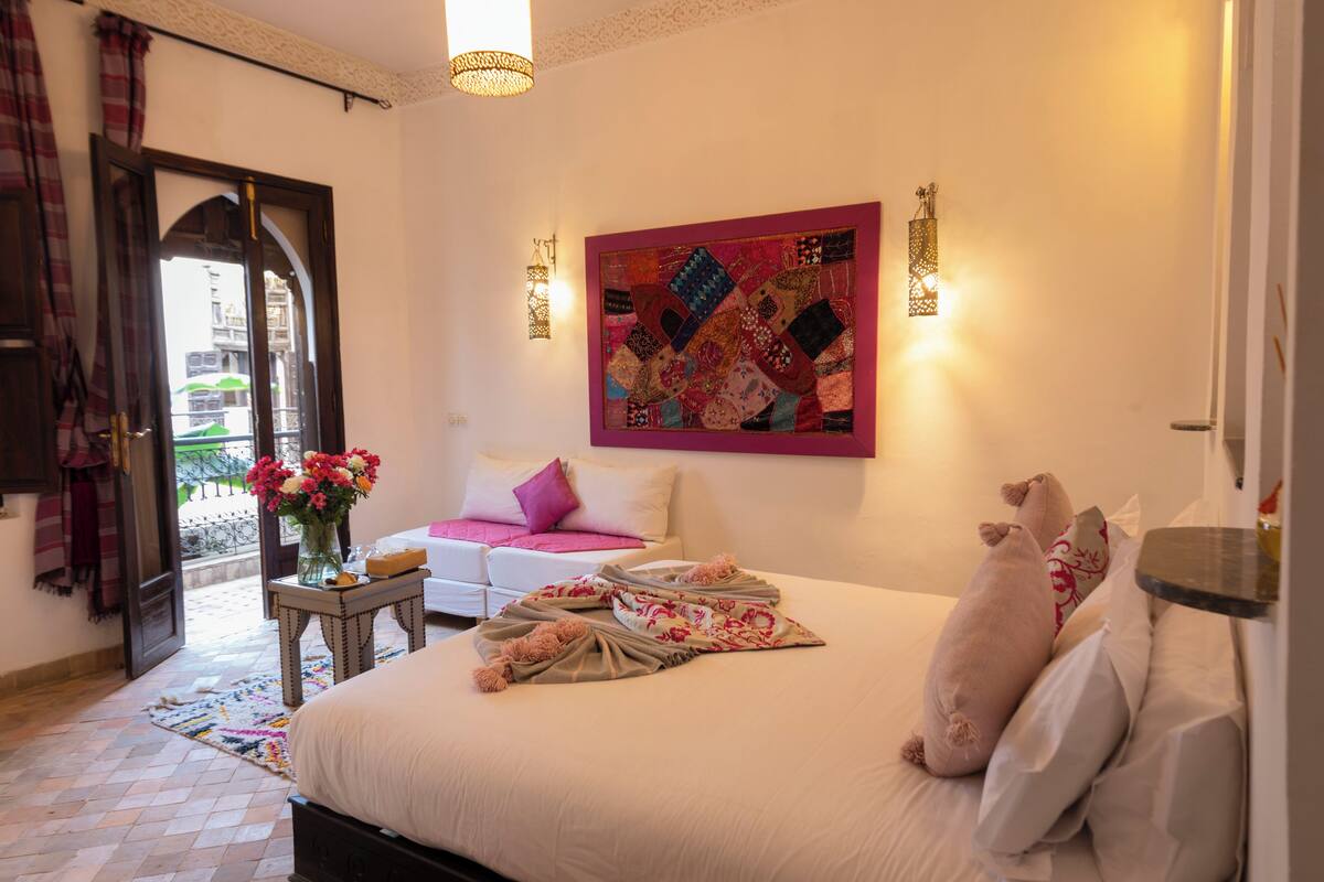 A bedroom with a bed, pillows, a quilt, a vase with flowers, a wall hanging, and a view through an open door.