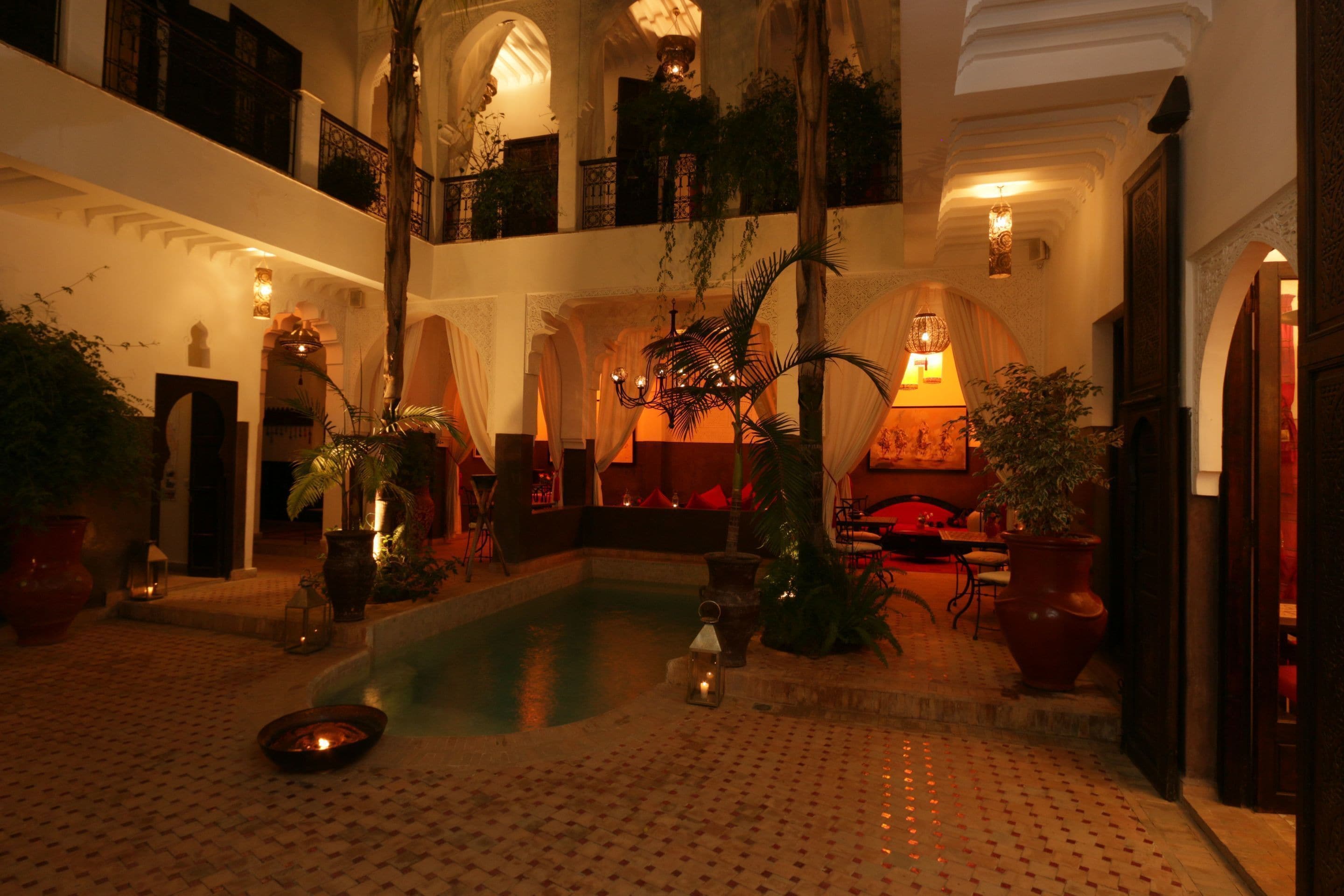 Un área de piscina interior lujosa con suelo de baldosas, rodeada de plantas en macetas y muebles elegantes.